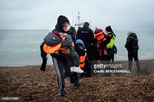 Migrant carries her children after being helped ashore from a RNLI lifeboat at a beach in Dungeness, on the south-east coast of England, on November...