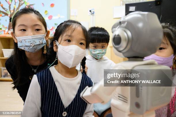 In this picture taken on November 23 young students interact with a 24.5 centimetre tall "Alpha Mini" robot who can dance, lead sing-a-longs, recite...