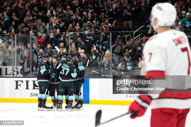 Jared McCann of the Seattle Kraken celebrates with teammates after scoring a goal as Brendan Smith of the Carolina Hurricanes looks on to tie the...