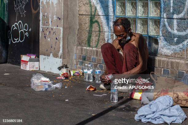 Homeless man sits on the sidewalk in front of the non-profit Midnight Mission's headquarters, while traditional Thanksgiving meals are served to...