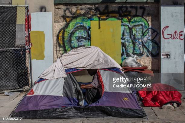 Homeless man sits in his tent as anofher sleeps on the sidewalks in front of the non-profit Midnight Mission's headquarters, while traditional...