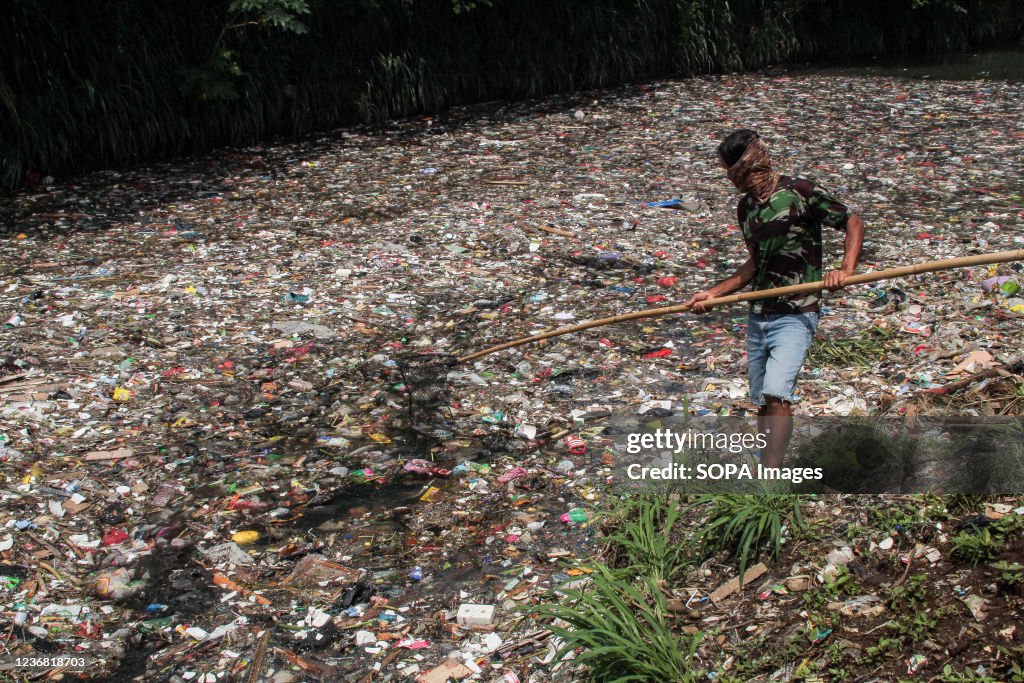 A man nets plastic waste to let water flow in the Bojong...