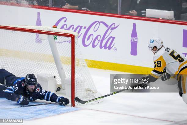 Jake Guentzel of the Pittsburgh Penguins shoots the puck into the empty net past a diving Mark Scheifele of the Winnipeg Jets for a third period goal...