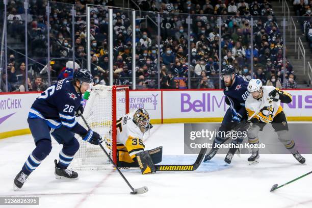 Blake Wheeler of the Winnipeg Jets plays the puck at the side of the net in front of teammate Pierre-Luc Dubois while goaltender Tristan Jarry and...