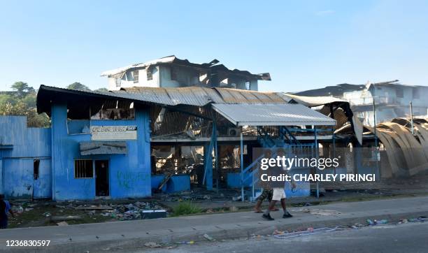 People walk past burnt-out buildings in Honiara on November 27 as a tense calm returned after days of intense rioting that left at least three dead...