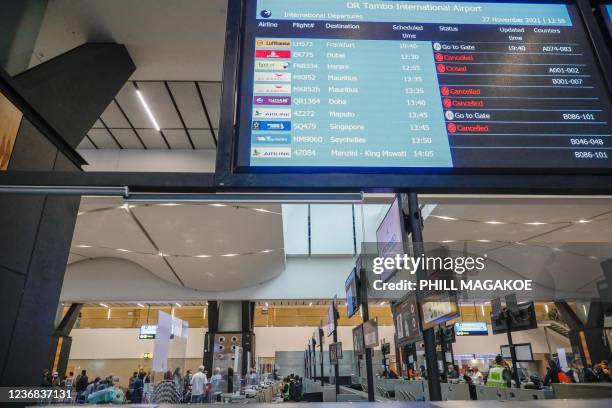 Airport staff assist travellers at various check-in counters while an electronic flight notice board displays some cancelled flights at OR Tambo...