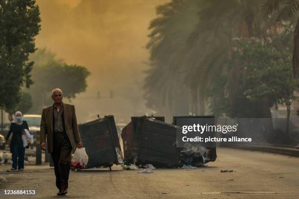 November 2021, Lebanon, Beirut: A Lebanese elderly man walks through smoke from burning trash and past garbage bins blocking a main highway in Beirut...
