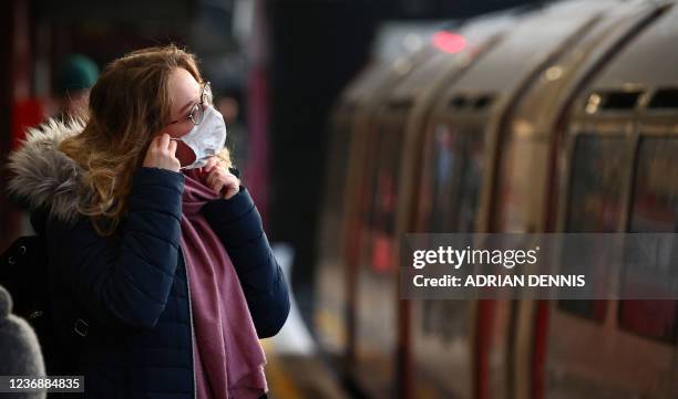 Woman adjusts her face mask at Barons Court Underground station in London on November 29, 2021. - Britain will require all arriving passengers to...