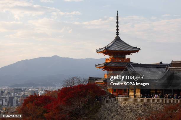 Three-storied Pagoda seen inside Kiyomizu-dera Buddhist temple in Kyoto surrounded by autumn colored leaves.