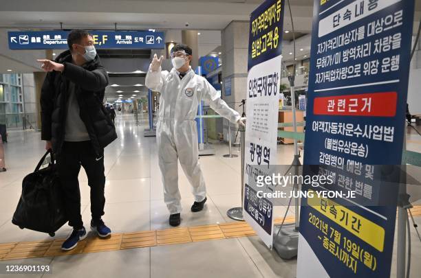Staff member wearing protective equipment guides a traveller at the arrival hall of Incheon International Airport on November 30 amid growing...