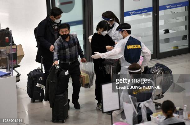Staff members wearing protective equipment guide travellers at the arrival hall of Incheon International Airport on November 30 amid growing concerns...