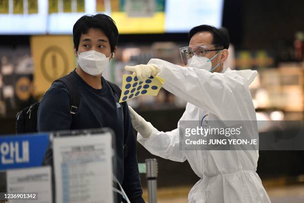 Staff member wearing protective equipment guides a traveller at the arrival hall of Incheon International Airport on November 30 amid growing...