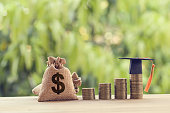 Black graduation cap, Hat and US dollar bag on rows of rising coins,  on a table. Education funding, financial concept. Depicts savings for child knowledge for future studies