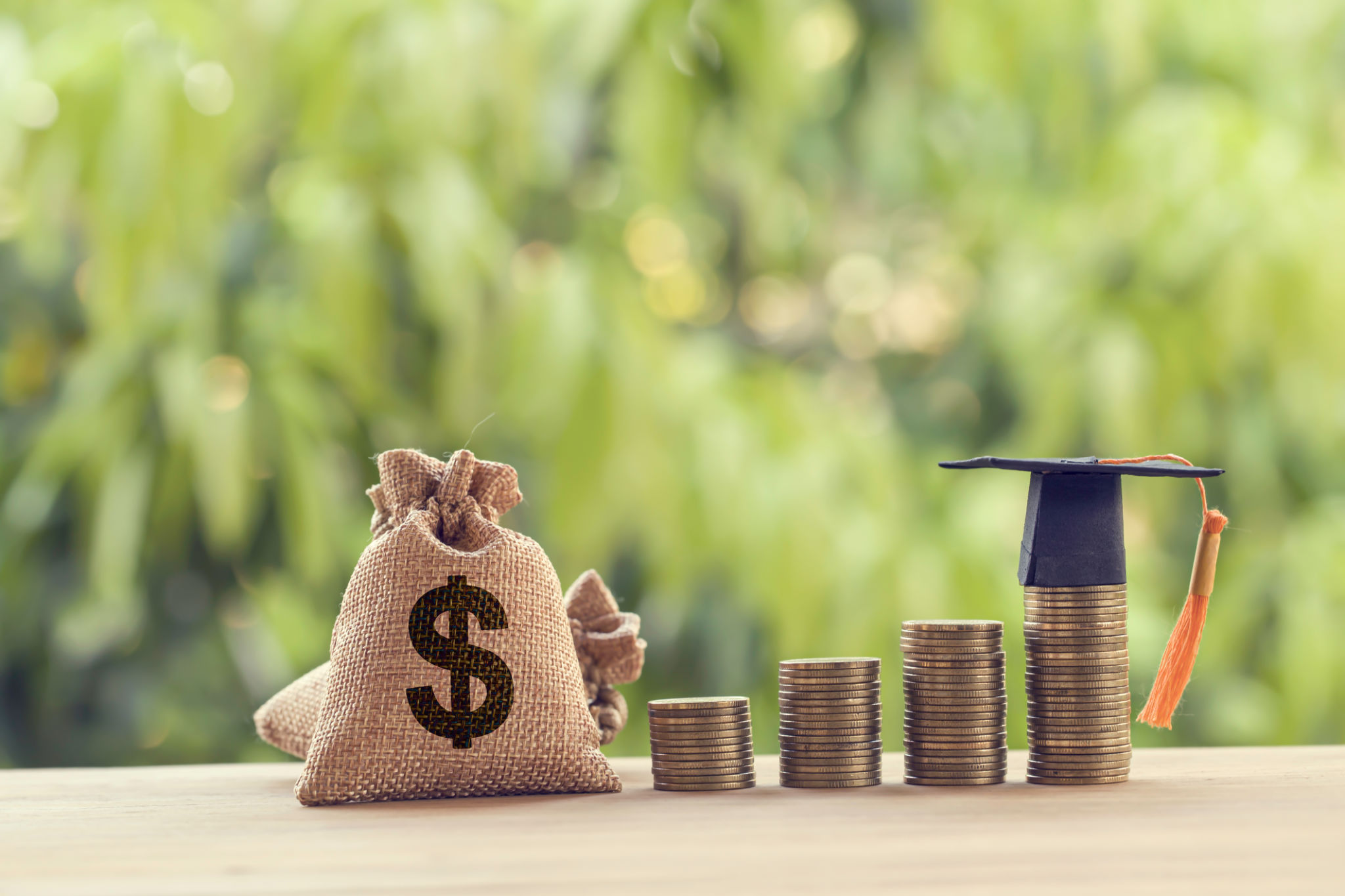 Black graduation cap, Hat and US dollar bag on rows of rising coins, on a table. Education funding, financial concept. Depicts savings for child knowledge for future studies Black graduation cap, Hat and US dollar bag on rows of rising coins, on a table. Education funding, financial concept. Depicts savings for child knowledge for future studies