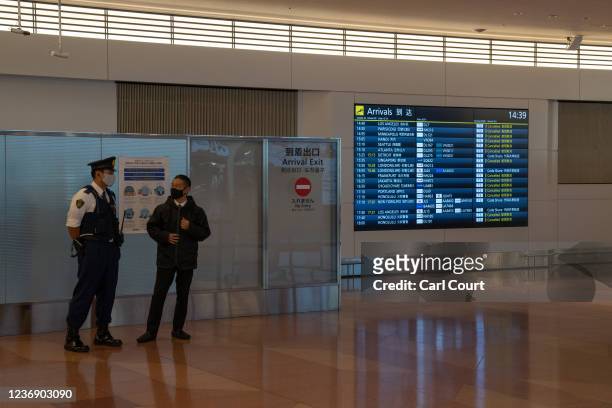Police officer talks with a man near an arrivals board displaying cancelled flights at Haneda Airport on November 30, 2021 in Tokyo, Japan. Japan has...
