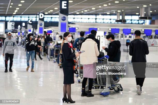 An employee wearing a protective mask assists travelers lining up at China Eastern Airlines Corp. Check-in counters at Narita Airport in Narita,...