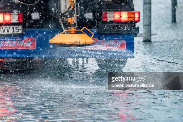 November 2021, Bavaria, Vilshofen: A vehicle of the winter service spreads salt on a street in the city centre. Winter has arrived in Bavaria with...