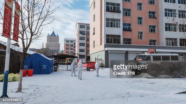 This photo taken on November 30, 2021 shows health workers in personal protective equipment standing guard outside a residental area which is...