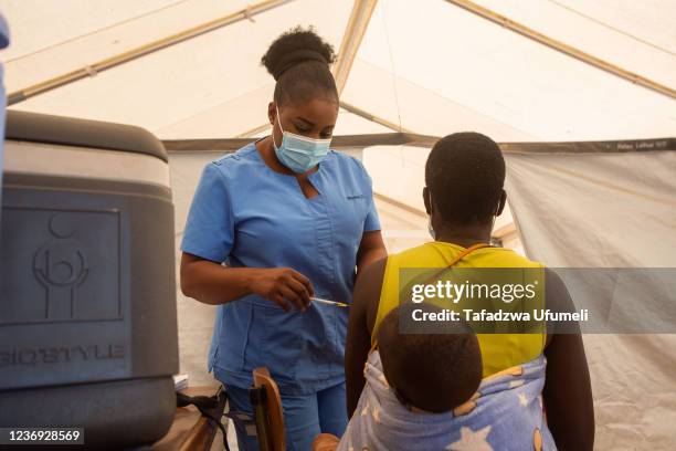 Nurse vaccinates a woman carrying a baby on her back at a hospital at Parirenyatwa group of hospitals on December 01, 2021 in Harare, Zimbabwe....