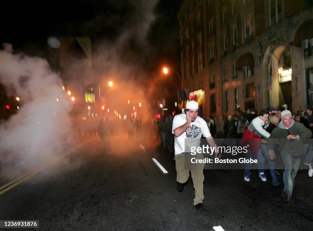 Red Sox fans run from the police as they shoot pepper spray to disperse the crowd on Beacon Streets following their victory over the St. Louis...