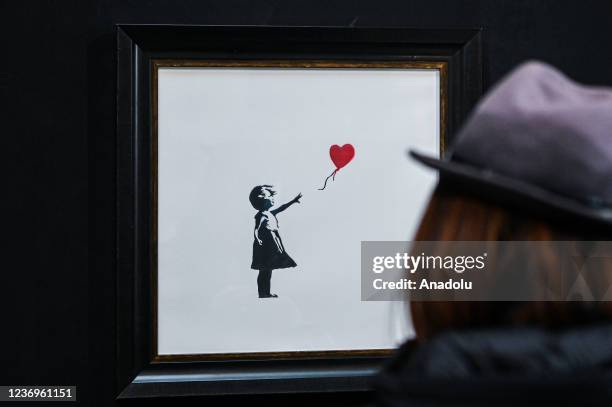 Woman looks to an artwork entitled 'Girl with Balloon - 2003' by Banksy during the The World of Banksy â The Immersive Experience exhibition opening...