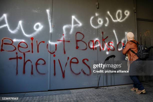 December 2021, Lebanon, Beirut: A Lebanese anti-government activist sprays slogans on the heavily fortified door of a local bank during a protest...