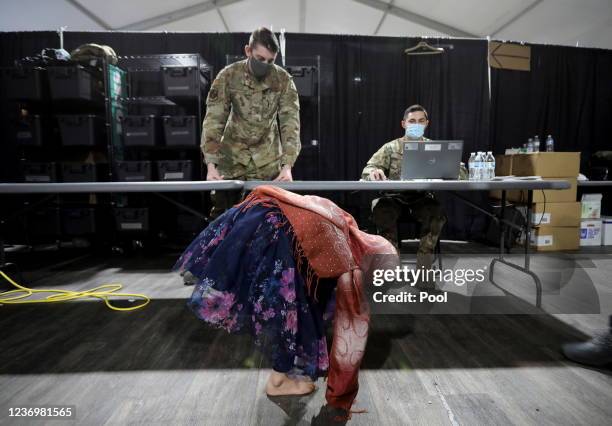An Afghan refugee girl tries on a pair of new shoes as military members that are assisting her look on at a distribution and donation center in...