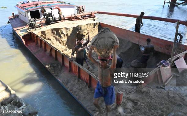 Workers carry soil accross river as dredgers are used to lift soil from the river for construction work in the town and the distortion continues in...