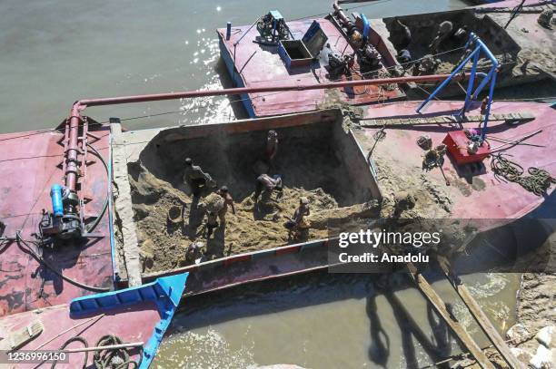 Workers carry soil accross river as dredgers are used to lift soil from the river for construction work in the town and the distortion continues in...