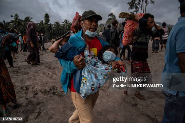 Villager carries a child as people salvage their belongings in an area covered in volcanic ash at Sumber Wuluh village in Lumajang on December 5...