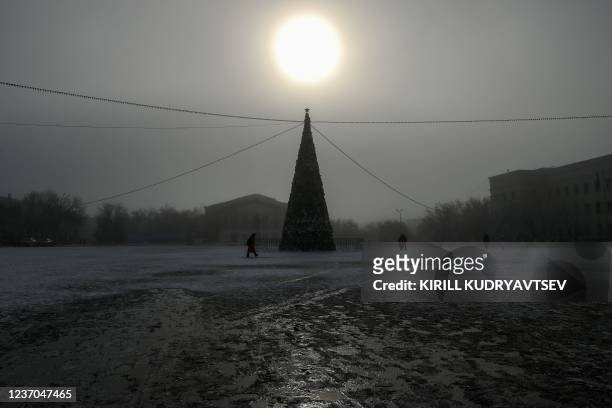 People walk past a Christmas tree during a winter foggy day in Baikonur city, near the Russian leased Kazakh Baikonur cosmodrome on December 6, 2021....