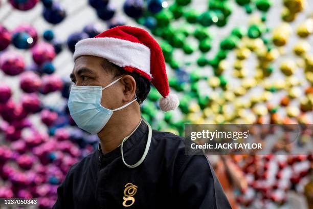 Man wearing a face mask and a Christmas Santa hat walks below decorations outside a shopping mall in Bangkok on December 6, 2021 as Thailand recorded...