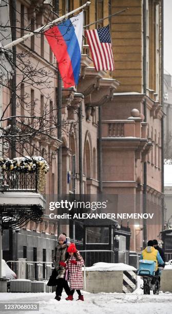 People walk by a Russian flag flying next to the US embassy building in Moscow on December 7, 2021. - Russian President Vladimir Putin and US...