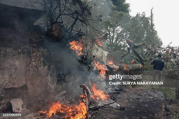 Man stands next to the burning debris of an IAF Mi-17V5 helicopter crash site in Coonoor, Tamil Nadu, on December 8, 2021. - A helicopter carrying...