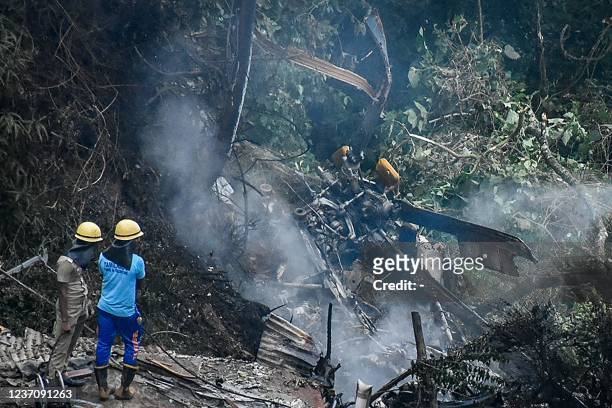 Firemen and rescue workers stand next to the debris of an IAF Mi-17V5 helicopter crash site in Coonoor, Tamil Nadu, on December 8, 2021. - A...