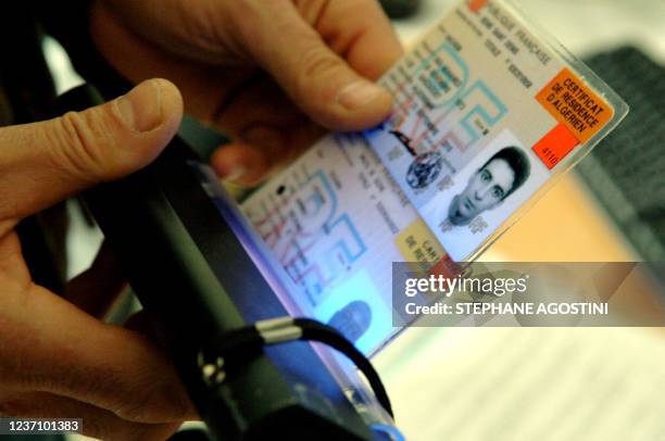 Un officier de la Police aux Frontières d'Ajaccio passe devant la presse, le 03 février 2006, deux fausses cartes de séjour françaises sous une lampe...