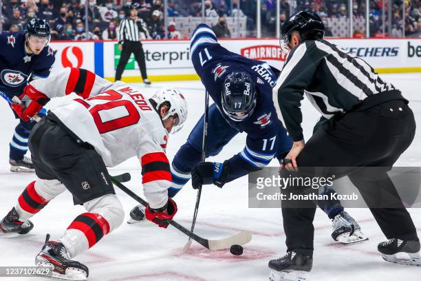 Michael McLeod of the New Jersey Devils and Adam Lowry of the Winnipeg Jets take a second period face-off at Canada Life Centre on December 03, 2021...