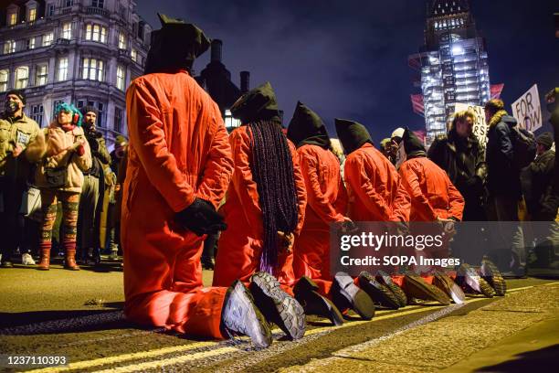 Protesters kneel on the ground while wearing prison costumes and black bags covering their faces in front of the crowd during the demonstration....