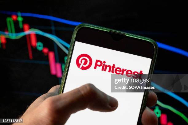 In this photo illustration the social media web and mobile application company Pinterest logo seen displayed on a smartphone with an economic stock...