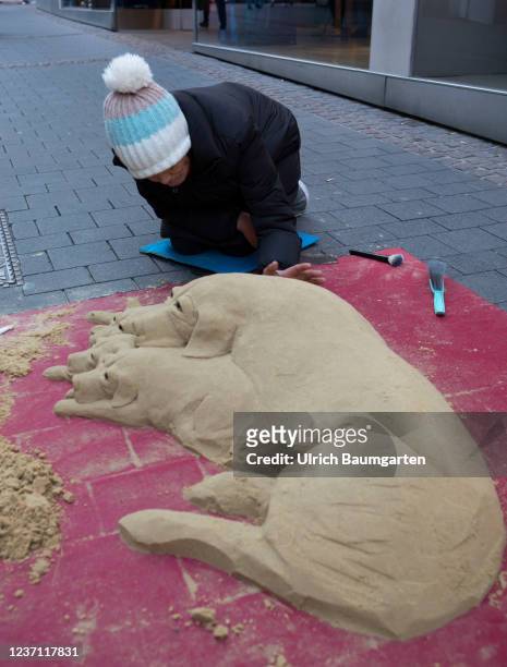 Woman working on a dog sand sculpture in the pre-Christmas pedestrian zone on December 09, 2021 in Bonn, Germany.