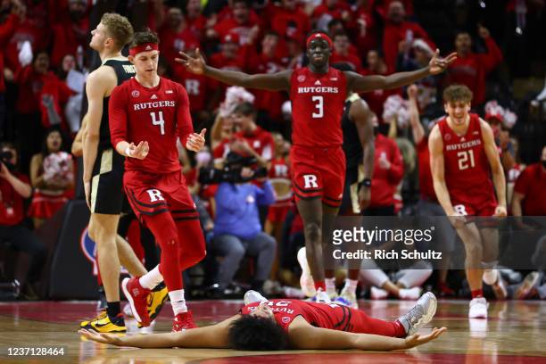 Ron Harper Jr. #24 of the Rutgers Scarlet Knights lies on the court after sinking a three-point shot as teammates Paul Mulcahy, Mawot Mag and Dean...