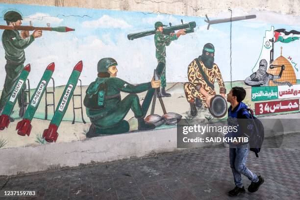 Child walks past a mural depicting soldiers firing rockets as Palestinians mark the 34th anniversary of the founding of the Islamist Hamas movement...