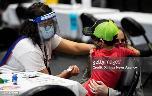Vaccinator wearing a face mask and a face shield prepares to administer the COVID-19 vaccine to a child at a vaccination site in Toronto, Canada, on...