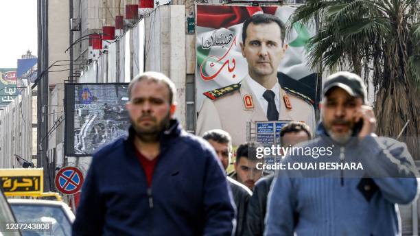 People walk before a giant billboard showing Syria's president Bashar al-Assad dressed in military uniform along a street in the capital Damascus on...