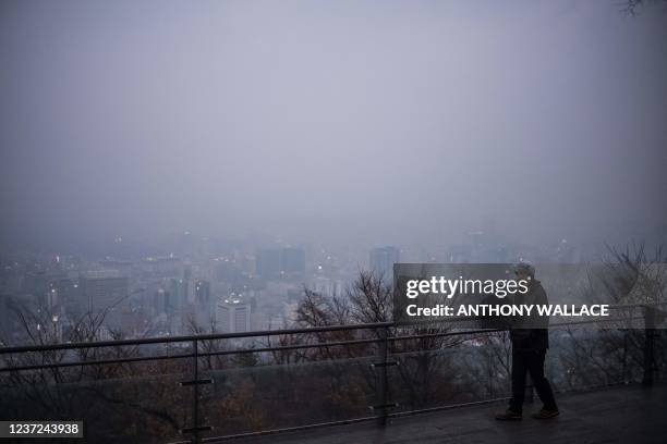 Man looks out towards buildings shrouded in haze as he visits the Namsan Tower on a polluted day in Seoul on December 15, 2021.