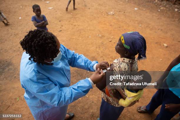 Woman gets vaccinated with an infant on her back at a shopping centre near Buwi Secondary School on December 15, 2021 in Chinhoyi, Zimbabwe. The...