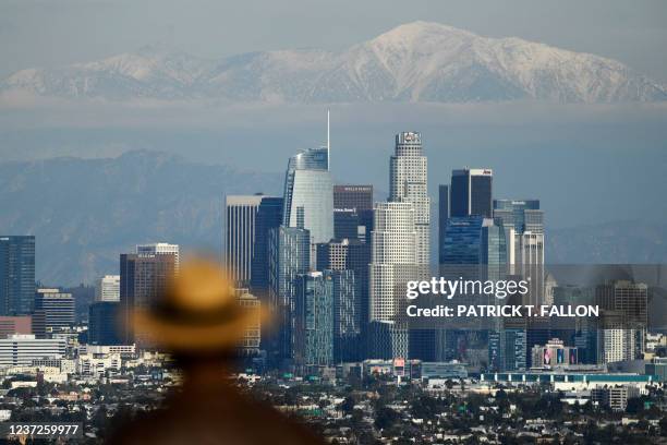 Person looks toward snow-topped mountains behind the Los Angeles downtown skyline following heavy rains, as seen from the Kenneth Hahn State...