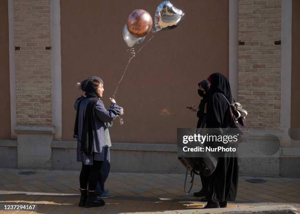Iranian young women talk to each other as one of them holds balloons while standing on a street-side out of a historical church in the city of...