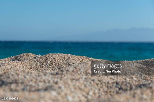 Closeup at the sand and the grains. Tourists as seen enjoying the sun, swimming, sunbathing and tanning at Paralia Lia beach in Mykonos island. A...