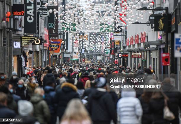 People are seen wearing face masks as they walk in a pedestrian street among shops and Christmas decorations in the city of Cologne, western Germany,...